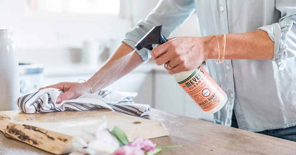 Hands holding a spray bottle and sponge wiping a kitchen counter